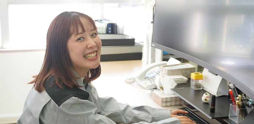 事務所のデスクで作業する代表取締役 佐藤綾華。レナトゥスの作業着を着ている